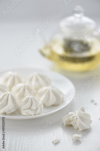 meringues in a plate with green tea in a kettle on a white background