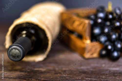 Bottle of red wine and grapes on wooden surface