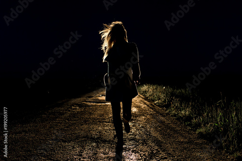 lonely young frightened woman on an empty night road runs away in the light of the headlights of her car