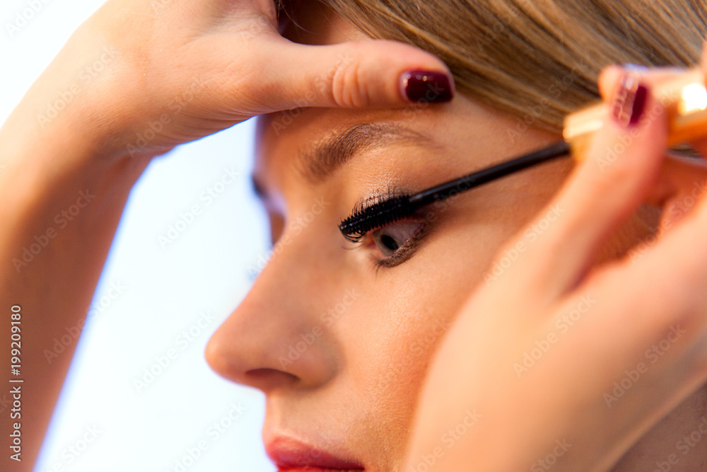 Obraz premium Hand holding a brush for mascara. Make-up artist makes up eyelashes for a blonde girl in the beauty studio close up