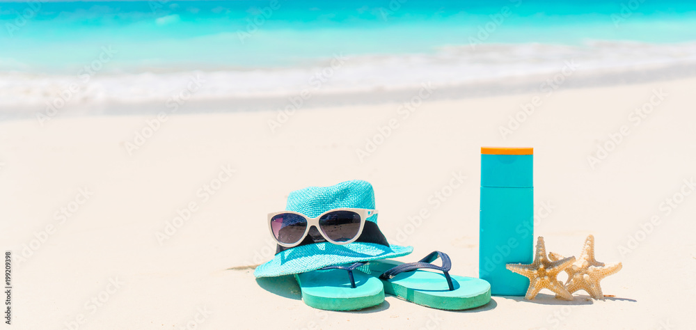 Suncream bottles, sunglasses, flip flop starfish on white sand background ocean