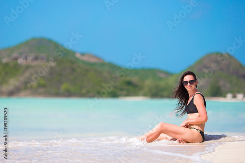 Woman sitting on beach laughing and enjoying summer holidays looking at the camera. Beautiful model in bikini sitting down.