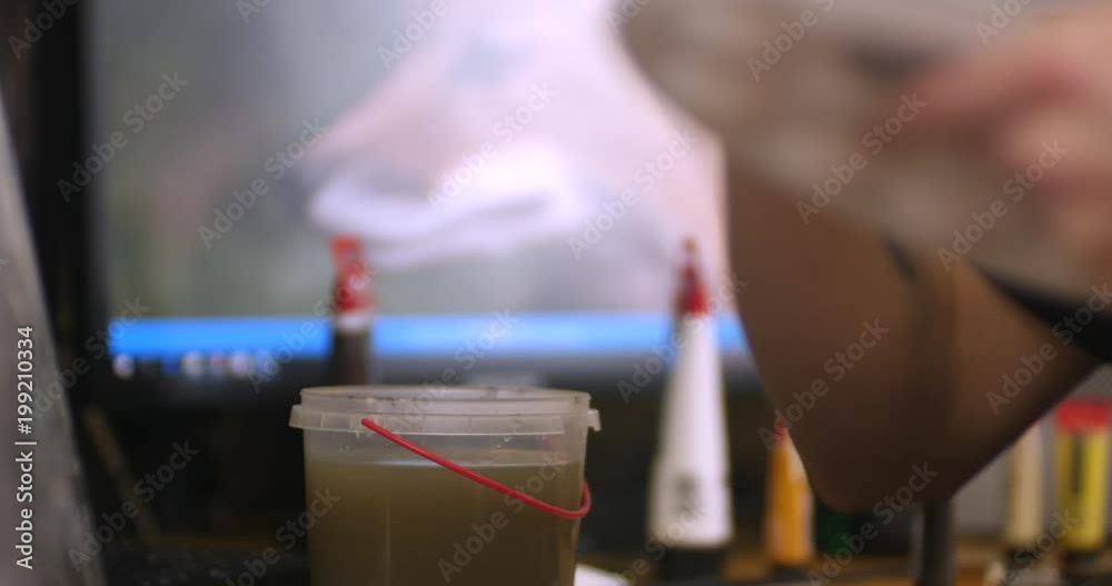 Closeup of a hand rinsing paintbrush in jar of water Closeup of a hand rinsing paintbrush in jar of water