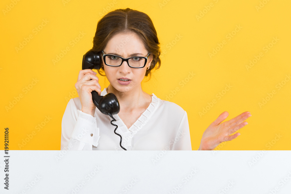 Portrait of confident beautiful angry young business woman with telephone with blank billboard on yellow background Portrait of confident beautiful angry young business woman with telephone with blank billboard on yellow background