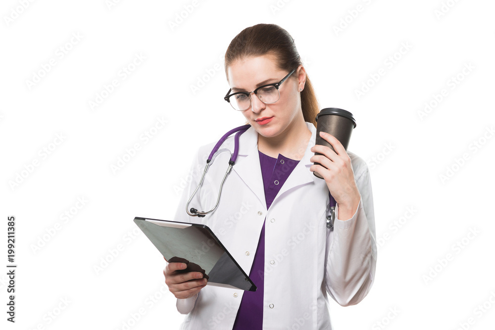 Attractive caucasian brunette confident female doctor standing in office with cup of coffee and tablet in her hands on white background Attractive caucasian brunette confident female doctor standing in office with cup of coffee and tablet in her hands on white background
