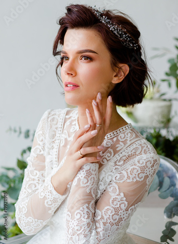 Portrait of a gentle bride. The woman is sitting in a white room with green leaves