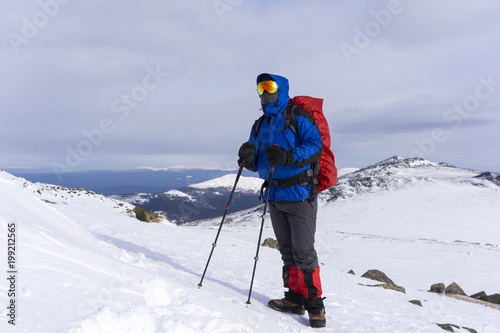 climber in mirror wind-proof glasses and a windproof mask with a backpack on a background of a winter mountain landscape