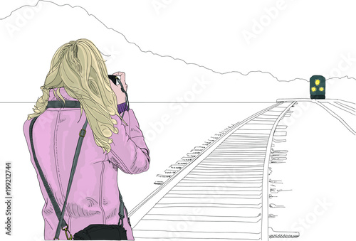 Young woman stands on train tracks to take a photo of a train approaching in the distance. Concept of outdoor adventure and photography journey.