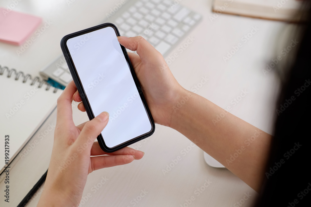 Blank screen mobile phone in female hands on desk Blank screen mobile phone in female hands on desk