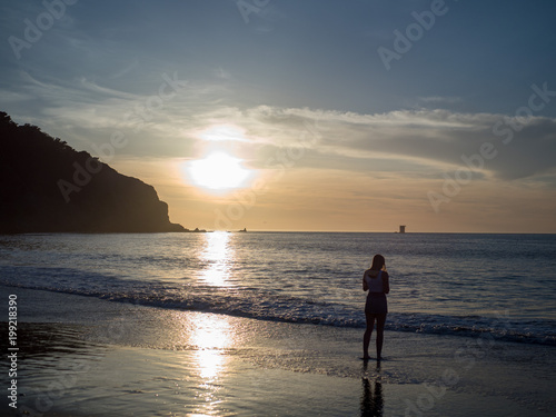 Woman observing the setting sun over the Pacific Ocean