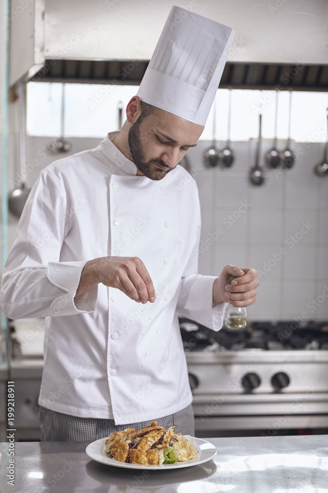 Chef sprinkling seasoning on food in plate at commercial kitchen Chef sprinkling seasoning on food in plate at commercial kitchen