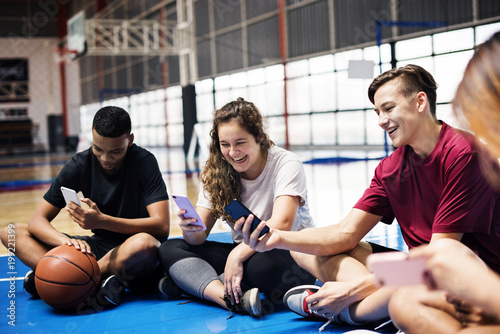 Group of young teenager friends on a basketball court relaxing and using smartphone