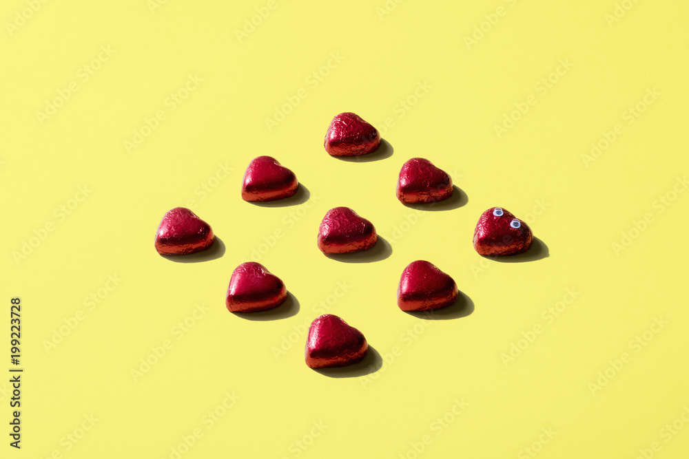High angle view of heart shape chocolates wrapped in red foil over yellow background High angle view of heart shape chocolates wrapped in red foil over yellow background