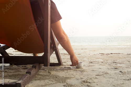 Man sitting in chair on beach with hand holding coffee