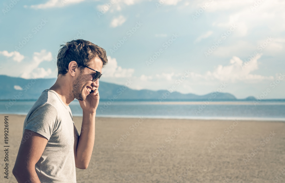 Handsome young male in glasses walking on the beach  and talking on mobile phone. Communication concept