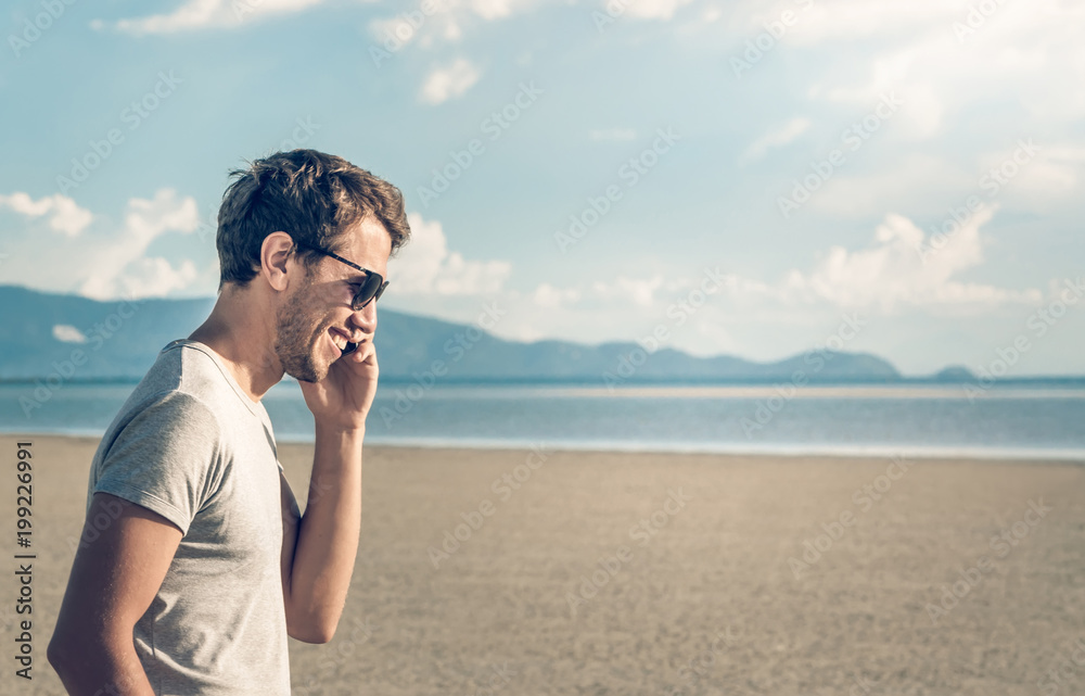 Handsome young male in glasses walking on the beach and talking on mobile phone. Communication concept Handsome young male in glasses walking on the beach and talking on mobile phone. Communication concept