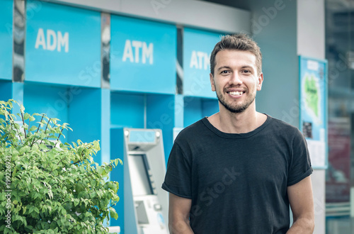 Portrait of handsome young man on atm machine background. Banking concept