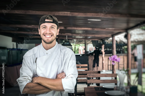 Portrait of a young smiling chef standing on the background of a summer restaurant