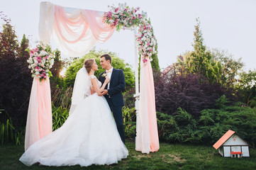 Beautiful newlyweds are hugging at a wedding ceremony. The wedding ceremony is green in the garden. Wedding decorations. Solar wedding in the park.