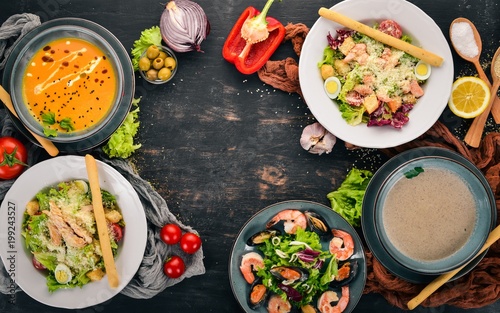 A set of healthy food in plates. Caesar salad, seafood, pumpkin soup and mushrooms. Top view. On a wooden background. Copy space.