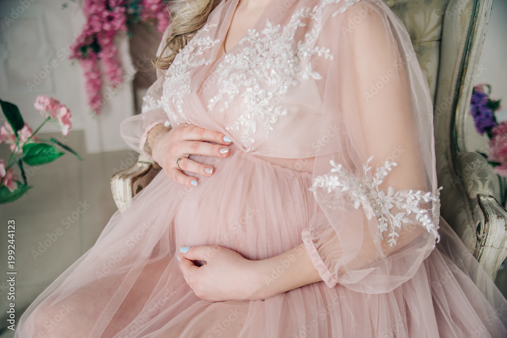 Pregnancy. The future mother in a luxurious negligee keeps her hands on her stomach.