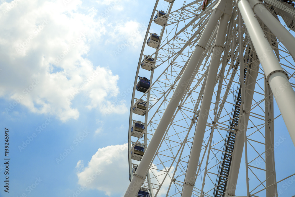 Giant Ferris wheel with numbered cabins in the park - Bright blue sky with sharp clouds behind it.