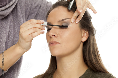 Makeup artist applying mascara on white background