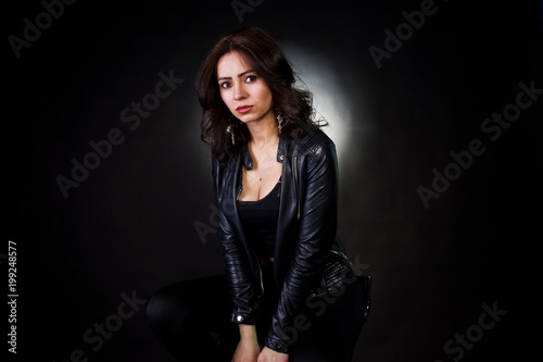Studio portrait of sexy brunette girl in black leather jacket against black background.