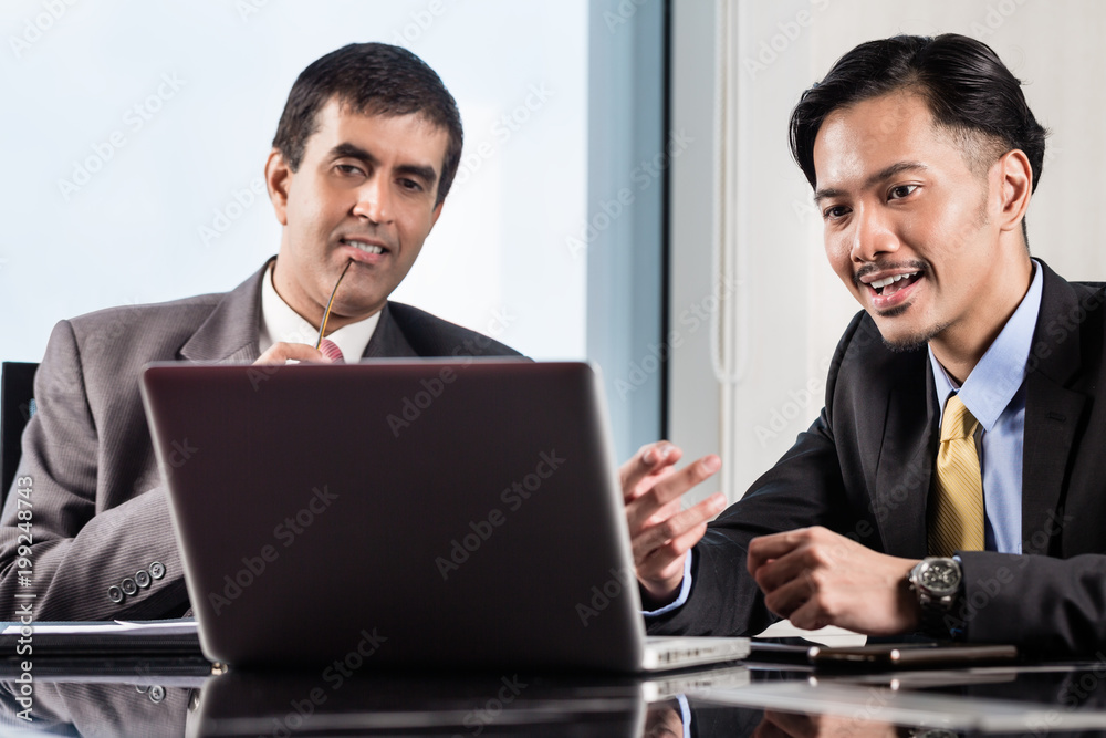 Senior manager and junior professional having business meeting and looking on notebook computer in office Senior manager and junior professional having business meeting and looking on notebook computer in office