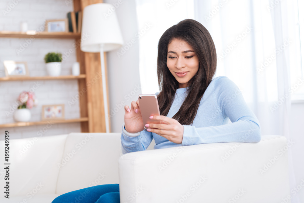 Active mailing. Thoughtful pretty woman smiling while holding smartphone Active mailing. Thoughtful pretty woman smiling while holding smartphone