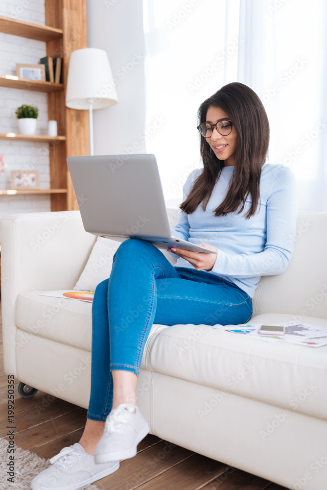 Learning process. Attractive positive female student studying on sofa while typing on laptop Learning process. Attractive positive female student studying on sofa while typing on laptop