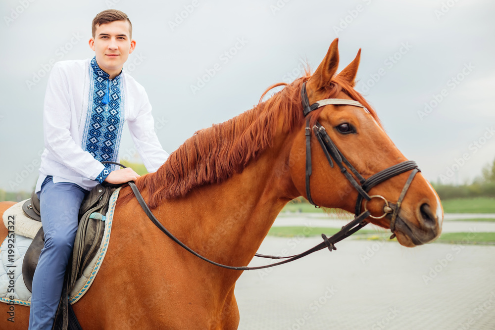 young guy in an embroidered shirt sits on a horse and looks at the camera lens young guy in an embroidered shirt sits on a horse and looks at the camera lens