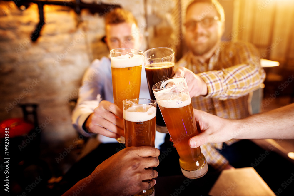 A group of young men clinking glasses with a beer in the sunny pub. A group of young men clinking glasses with a beer in the sunny pub.