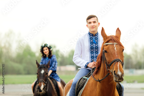 guy sits on a horse and looks at the camera lens on the background of his girl who sits on a horse