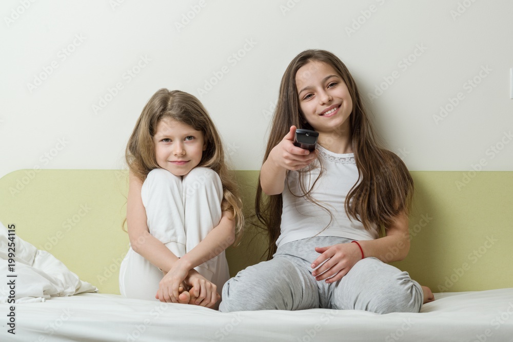 Children sitting at home in bed and watching TV. In the hands holding tv remote