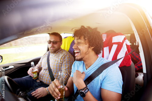 Portrait of drunk young afro-american man laughing and driving with a beer in hands while his friends having fun in the car.