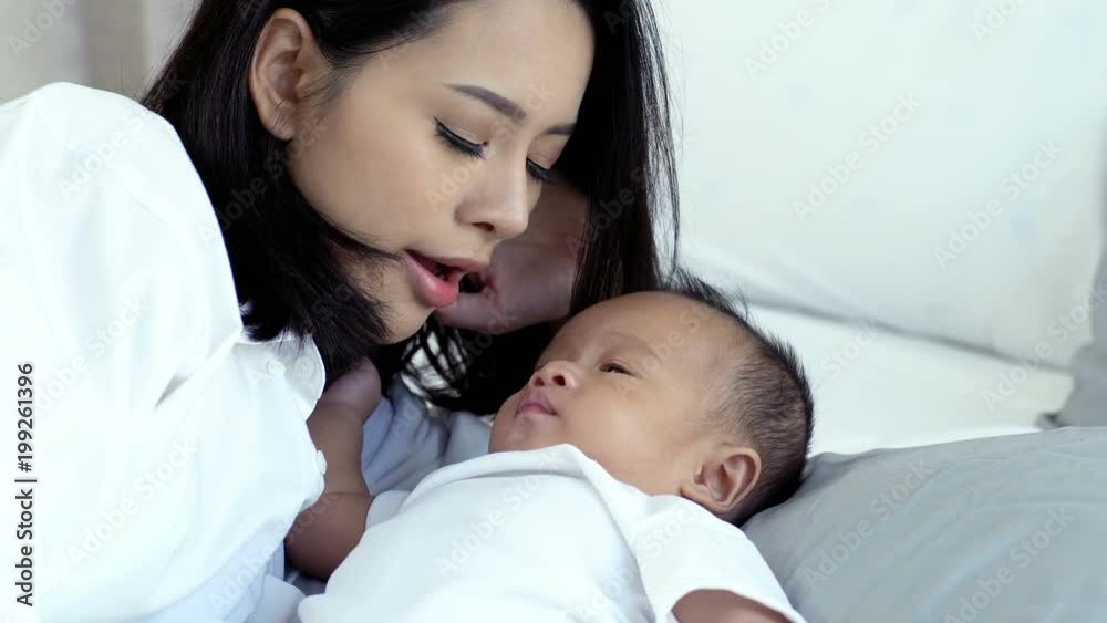 Young beautiful Asian mother caring and playing with her baby in the bedroom on a bright morning sunshine Young beautiful Asian mother caring and playing with her baby in the bedroom on a bright morning sunshine