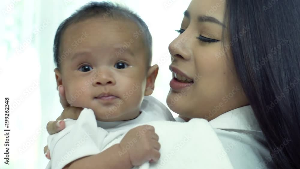 Young beautiful Asian mother caring and playing with her baby in the bedroom on a bright morning sunshine Young beautiful Asian mother caring and playing with her baby in the bedroom on a bright morning sunshine