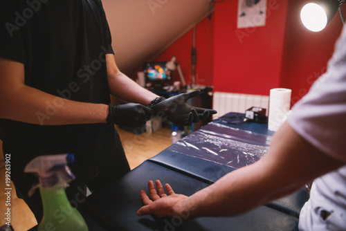 Tattoo artists putting black rubber gloves on and getting ready to tattoo customers arm.