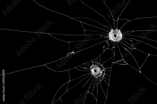 Two bullet holes on window glass cracks isolated on black background.