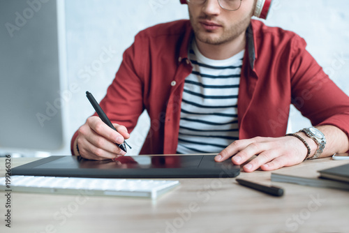 Young illustrator sitting by table with graphic tablet