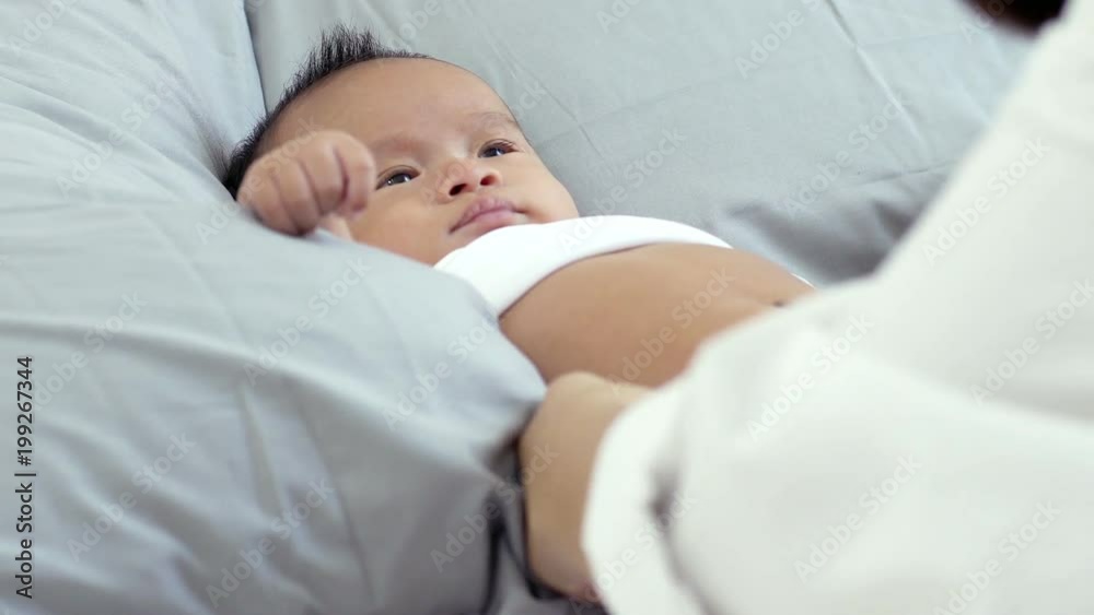 Young beautiful Asian mother caring and playing with her baby in the bedroom on a bright morning sunshine Young beautiful Asian mother caring and playing with her baby in the bedroom on a bright morning sunshine