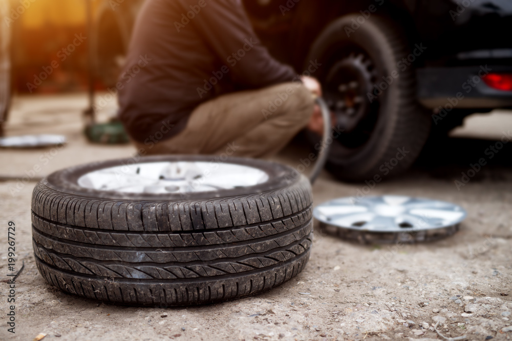 New tire laying on the pavement near the mechanic ready to replace the one on a car. New tire laying on the pavement near the mechanic ready to replace the one on a car.