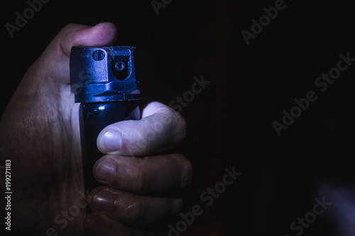 a man's hand holds a gas pepper spray in the dark, a black background. concept of safety and self-defense photo