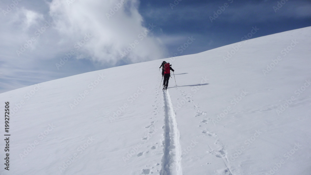 two backcountry skiers on a tour in the Austrian Alps and putting in new tracks on their way to the summit