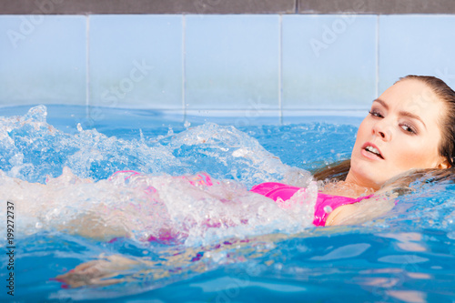 Woman in pink swimsuit swimming in blue pool on her back
