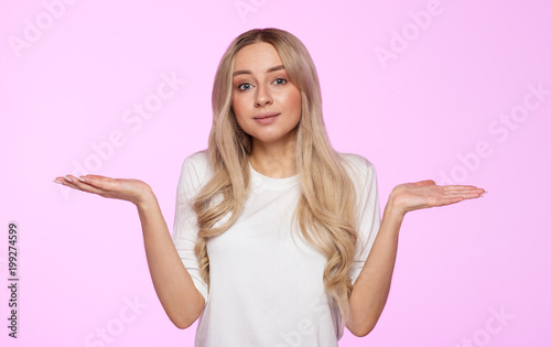 Studio portrait of cute puzzled young woman shrugs shoulders, does not know what happened. Pretty woman doubting isolated on pink background