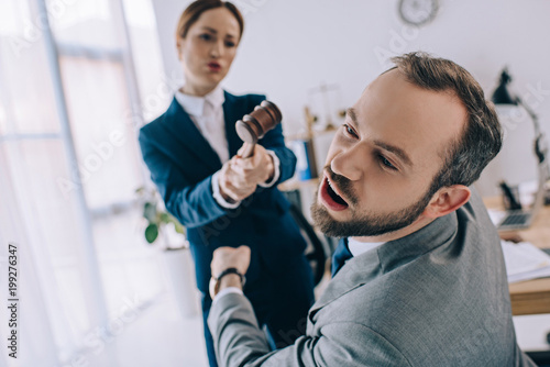 selective focus of lawyer pretending to hit colleague with gavel in hands in office