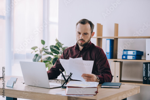 portrait of businessman doing paperwork at workplace with laptop in office