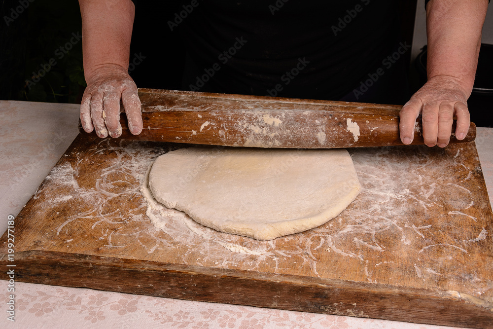 An old grandmother cleansing a dough with a shaft on a dark background An old grandmother cleansing a dough with a shaft on a dark background
